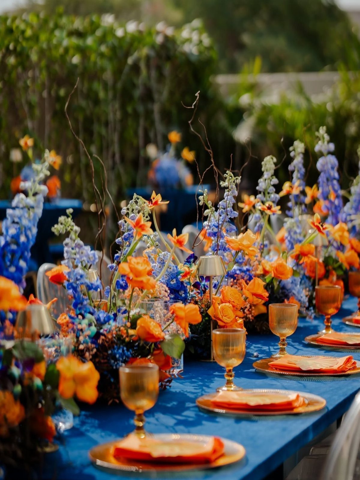 10 Blue Color Palette Wedding Ideas for Every Season 5 Blue table setting with orange napkins and tall blue and orange floral arrangements.