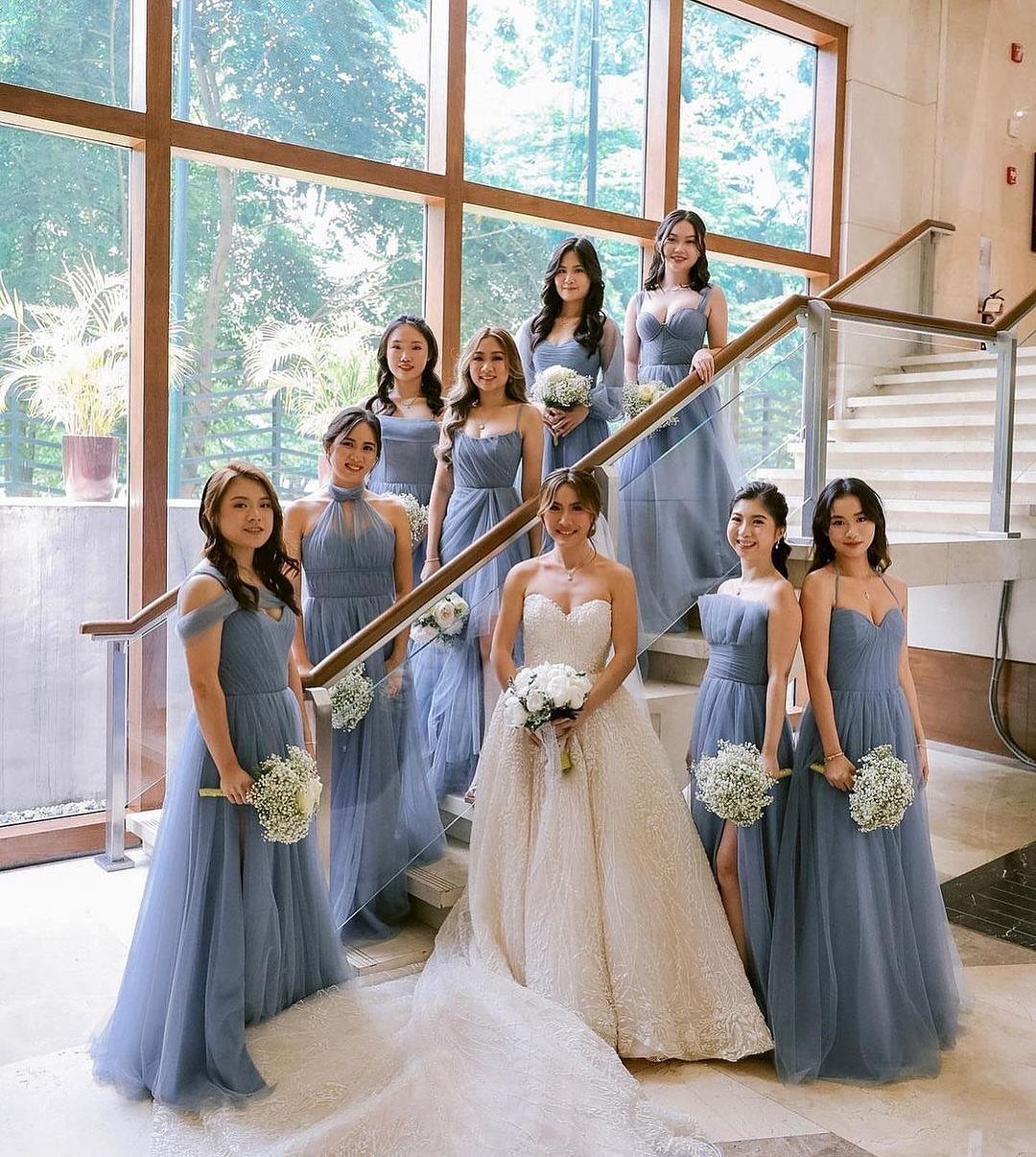 10 Blue Color Palette Wedding Ideas for Every Season 1 Bridesmaids in dusty blue dresses posing with a bride on a staircase holding white bouquets.