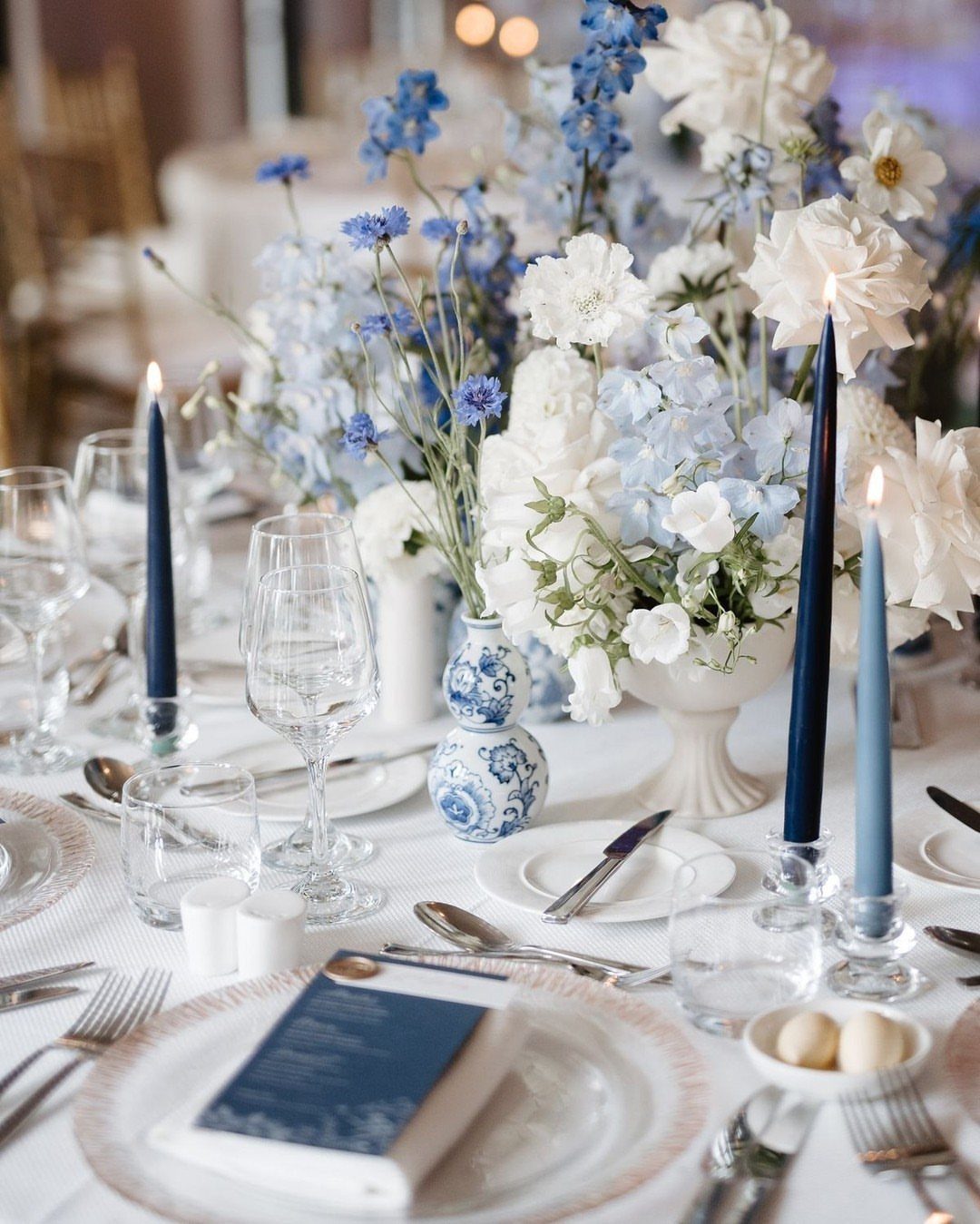 10 Blue Color Palette Wedding Ideas for Every Season 10 White and light blue flowers arranged with blue taper candles on a formal wedding table.
