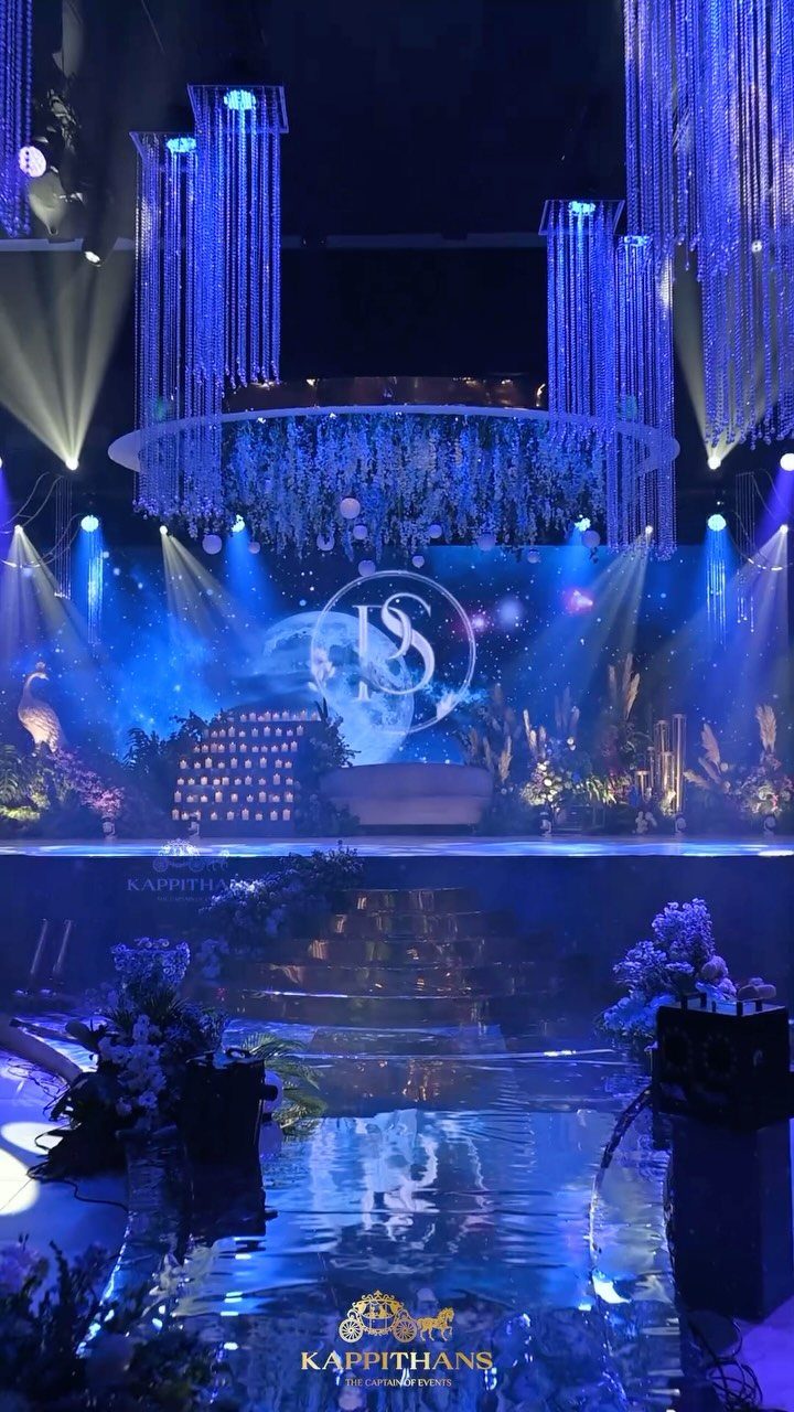 10 Blue Color Palette Wedding Ideas for Every Season 3 A wedding stage decorated with blue lights, hanging crystals, and floral arrangements on a reflective floor.