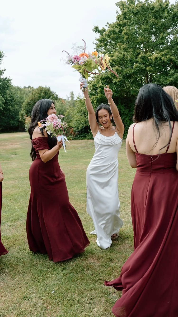 10 Burgundy Wedding Theme Ideas for Tables, Cakes and Attire 3 Three women celebrating outdoors, two wearing long burgundy dresses and one in a white dress.