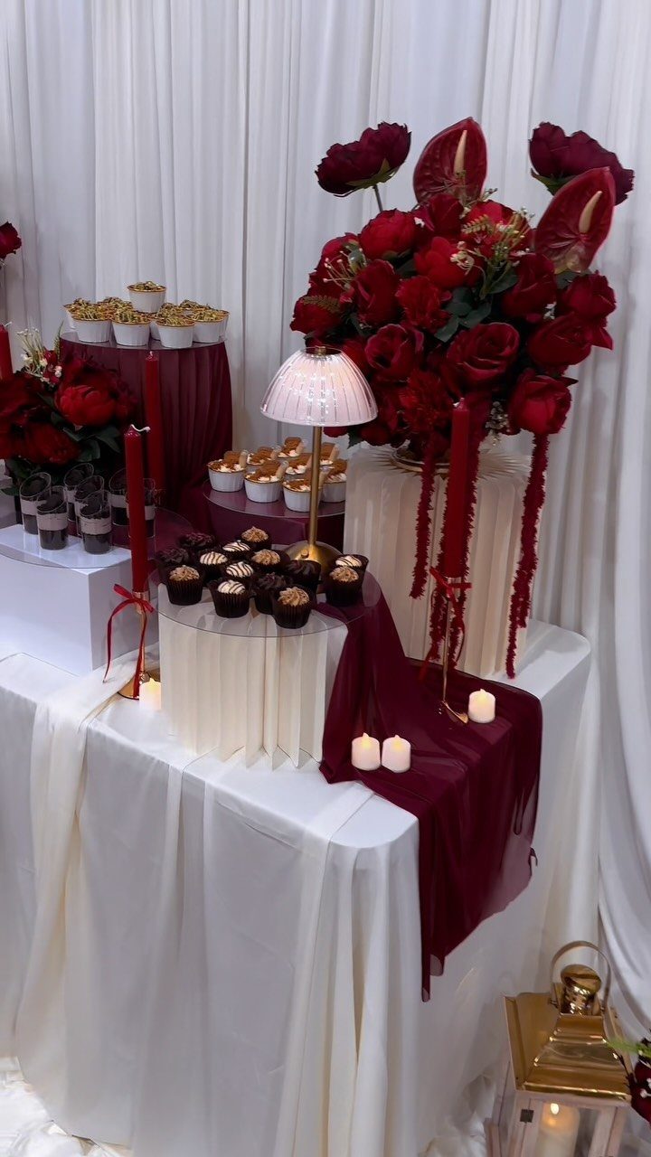 10 Burgundy Wedding Theme Ideas for Tables, Cakes and Attire 9 A dessert table featuring burgundy fabric, red floral arrangements, and small cupcakes on white stands.