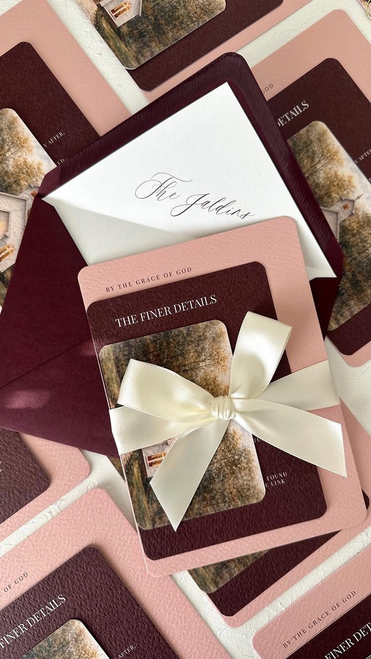 10 Burgundy Wedding Theme Ideas for Tables, Cakes and Attire 6 Burgundy and pink wedding invitations tied with a cream satin ribbon bow on a dark envelope.
