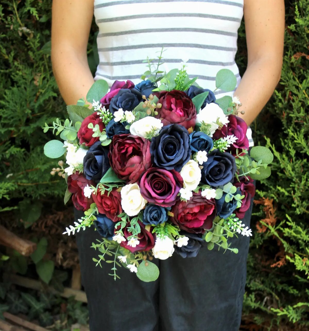10 Burgundy Wedding Theme Ideas for Tables, Cakes and Attire 4 A bouquet of burgundy, navy blue, and white roses with green eucalyptus leaves held by a person.