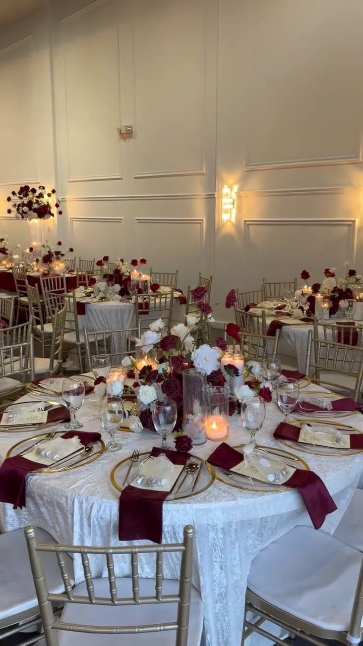 10 Burgundy Wedding Theme Ideas for Tables, Cakes and Attire 1 Banquet tables decorated with burgundy napkins, gold plates, and red and white floral centerpieces.