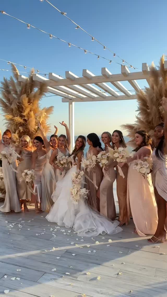 Bridesmaids in champagne dresses holding cream flower bouquets under a white pergola at sunset.