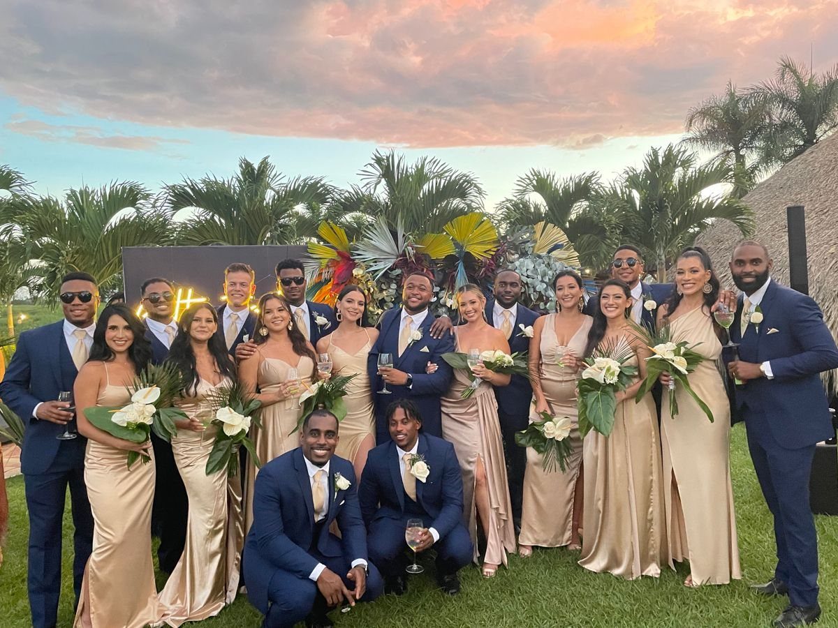 Wedding party in navy suits and champagne satin dresses posing outdoors at sunset.