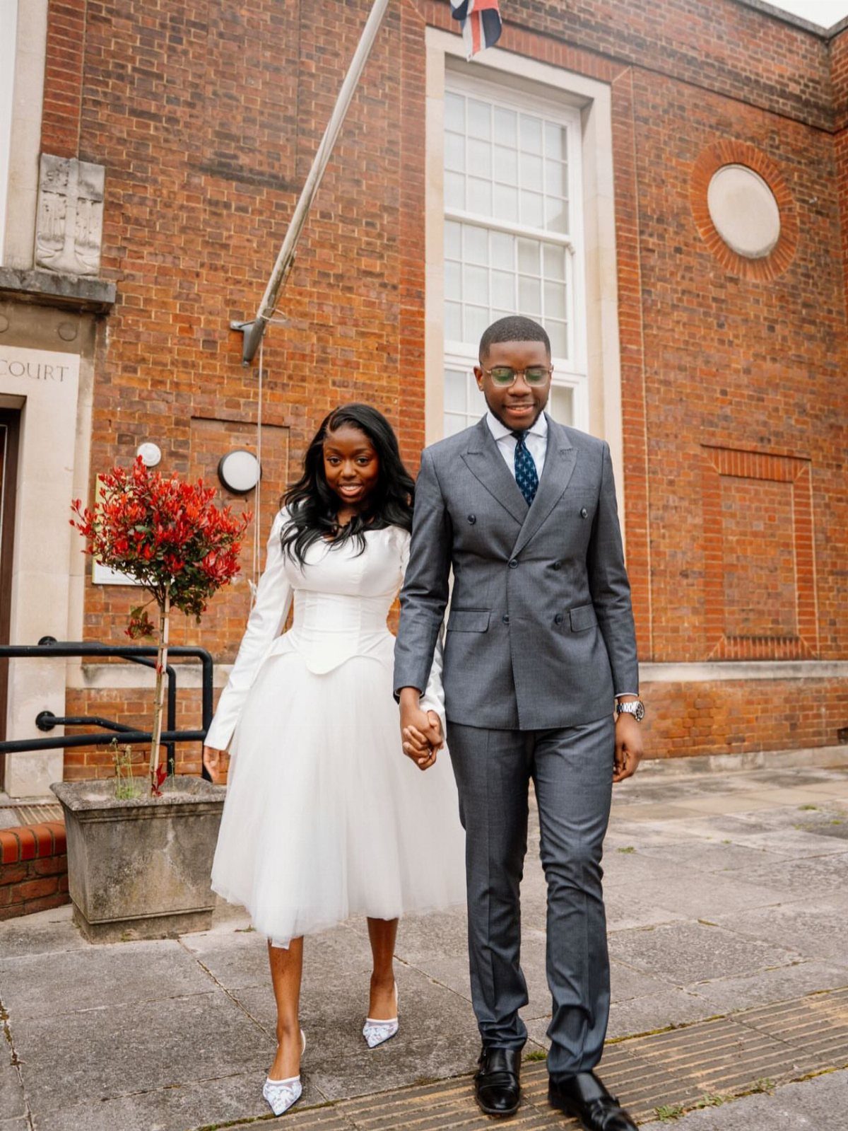 A woman in a white flared midi dress and a man in a grey suit walking together.