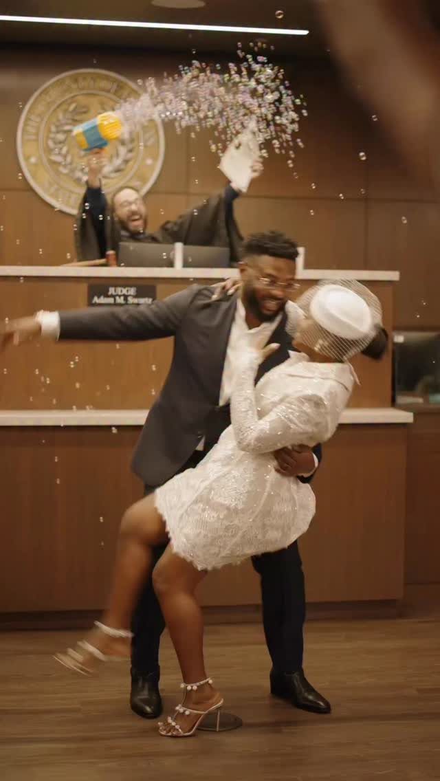 A man dips a woman in a white lace dress amidst flying confetti in a courtroom.