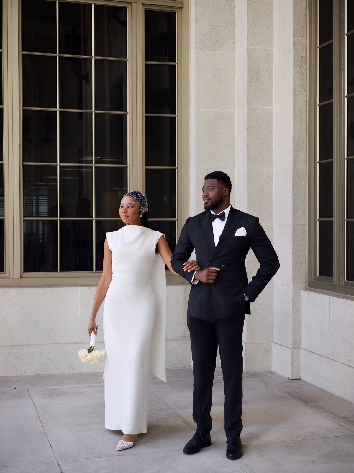 A woman in a white sleeveless crepe gown and a man in a black tuxedo posing together.
