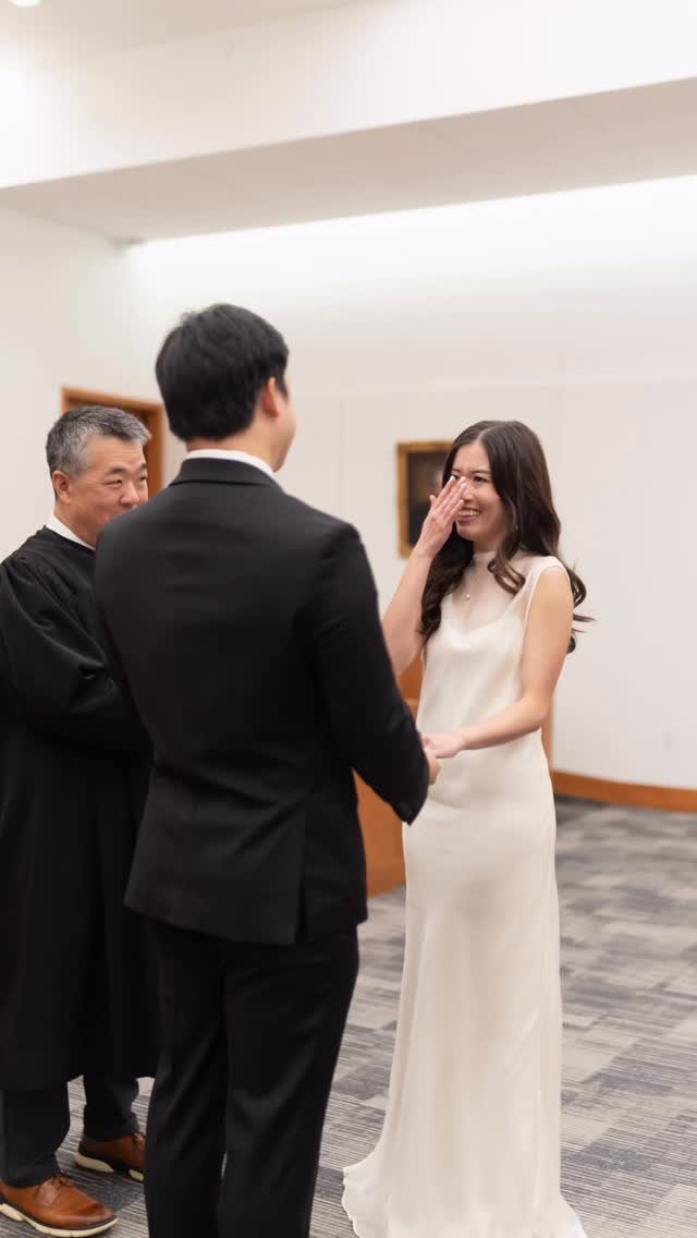 A bride in a white sleeveless gown holds hands with a groom in a black suit.