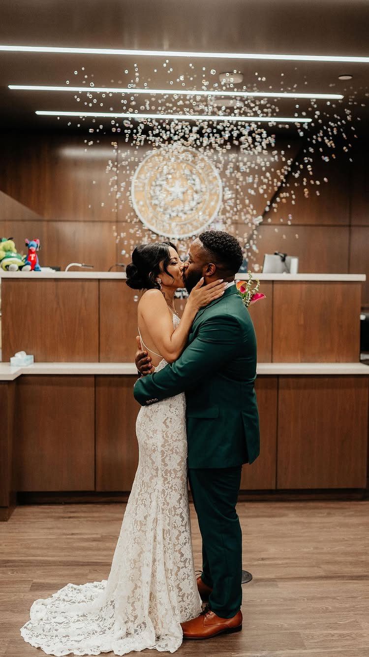 A bride in a white lace wedding dress and a groom in a green suit kissing.
