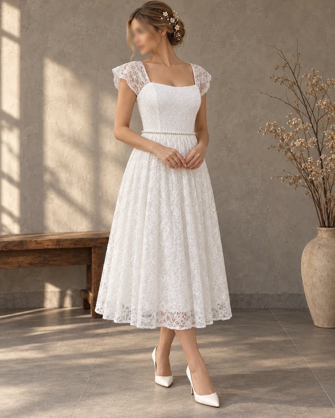 A woman posing in a white lace midi wedding dress and white high heels.