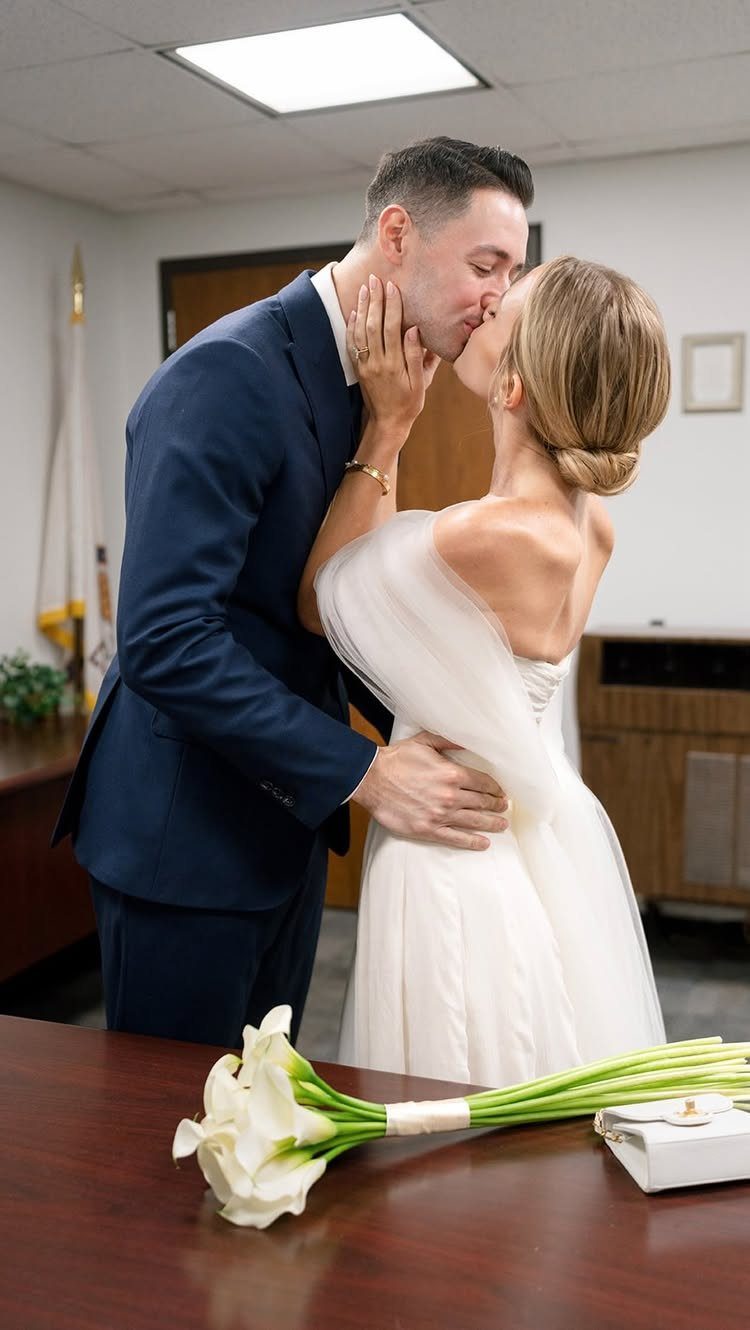 A bride in a white strapless dress and a groom in a navy suit kissing.