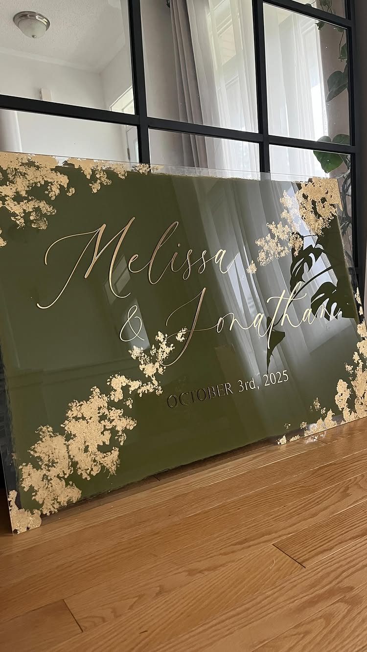 Dark Green Wedding: 13 Ideas for a Forest Reception 12 A dark green wedding sign with gold lettering and floral accents on a wooden floor.