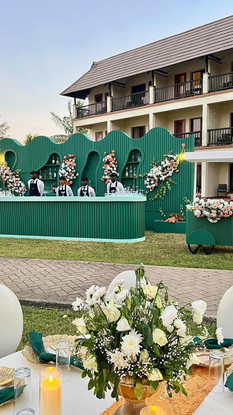 Dark Green Wedding: 13 Ideas for a Forest Reception 13 White floral centerpieces and lit candles sit on a table before a dark green outdoor bar.