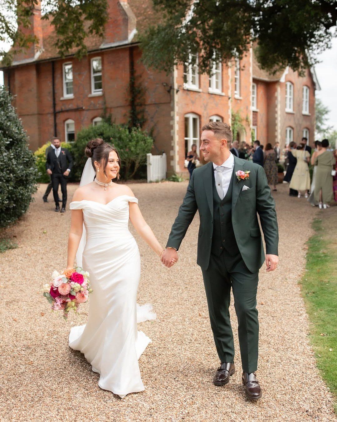 Dark Green Wedding: 13 Ideas for a Forest Reception 4 A bride and groom in a dark green suit walk together on a gravel path.