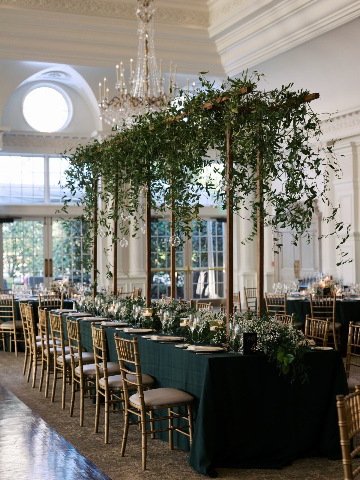Dark Green Wedding: 13 Ideas for a Forest Reception 9 Gold Chiavari chairs lined up along a long table with dark green linens and greenery.