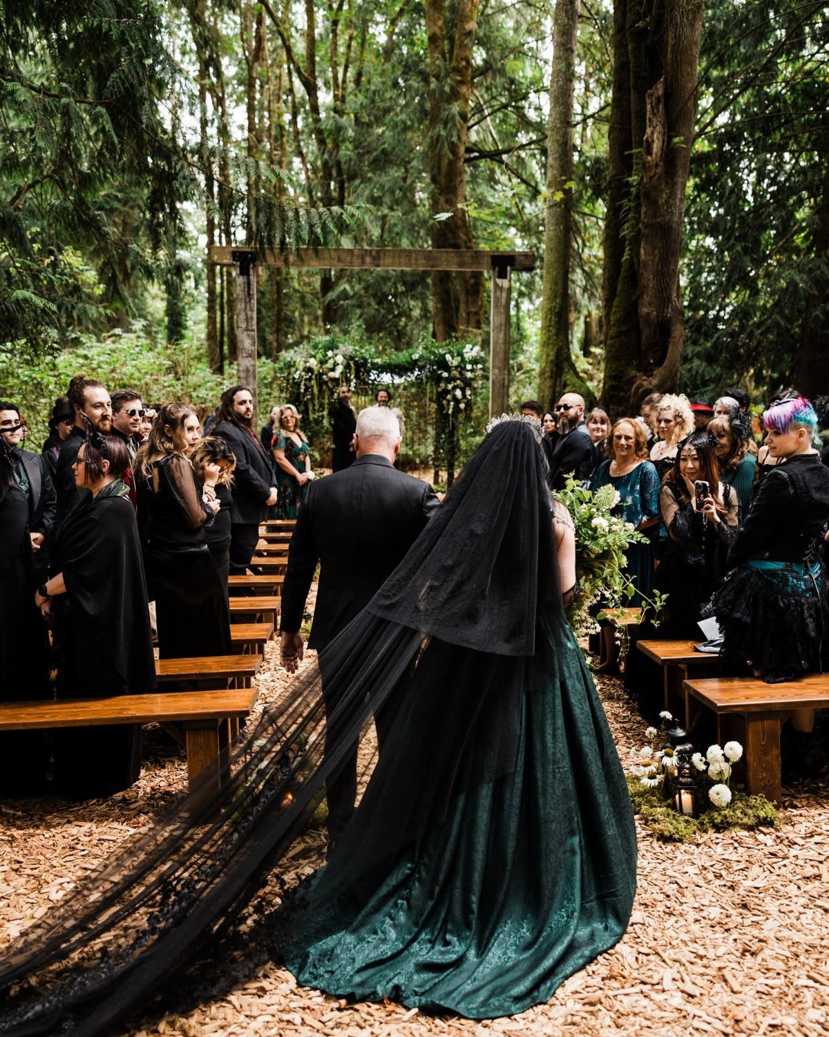 Dark Green Wedding: 13 Ideas for a Forest Reception 11 A bride in a dark green wedding dress and black veil walks down a forest aisle.