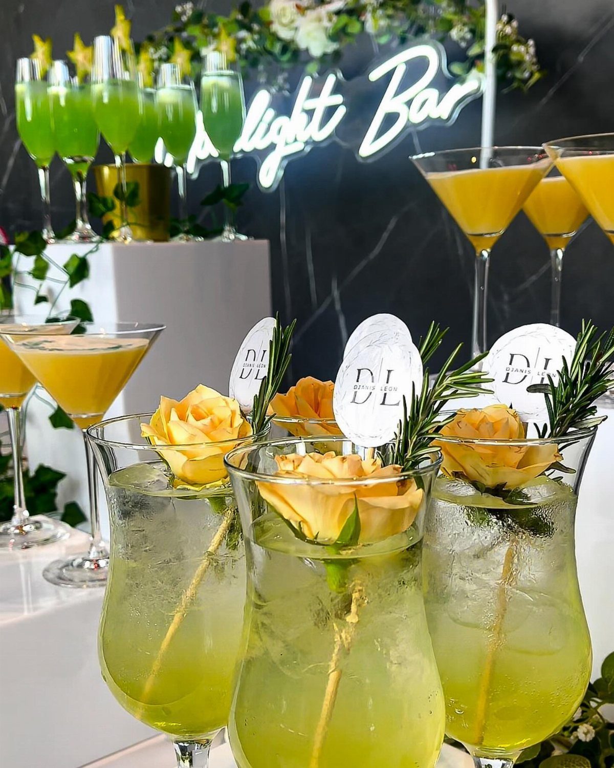 Dark Green Wedding: 13 Ideas for a Forest Reception 6 Cocktail glasses garnished with yellow roses and rosemary sprigs on a bar counter.