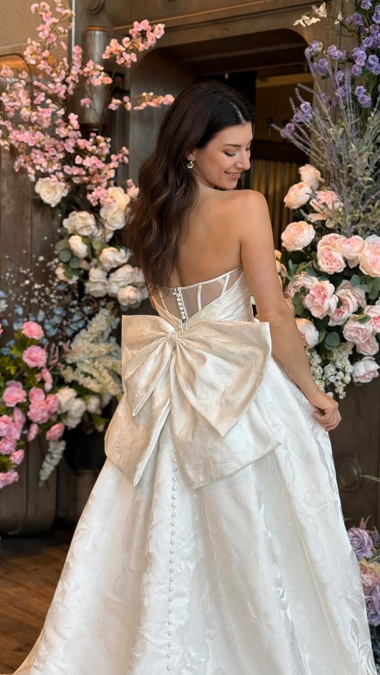 Woman in a white wedding dress with a large satin bow on the back.