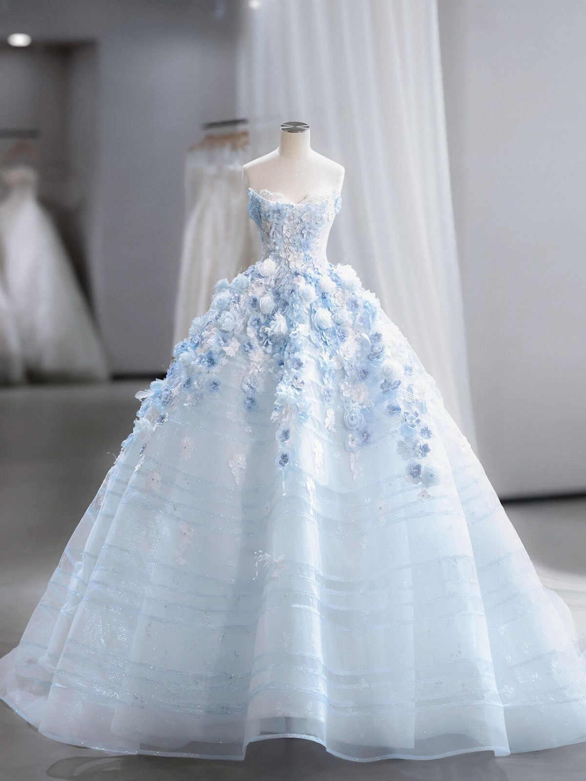 A light blue strapless ball gown decorated with large 3D floral appliqués on a mannequin.
