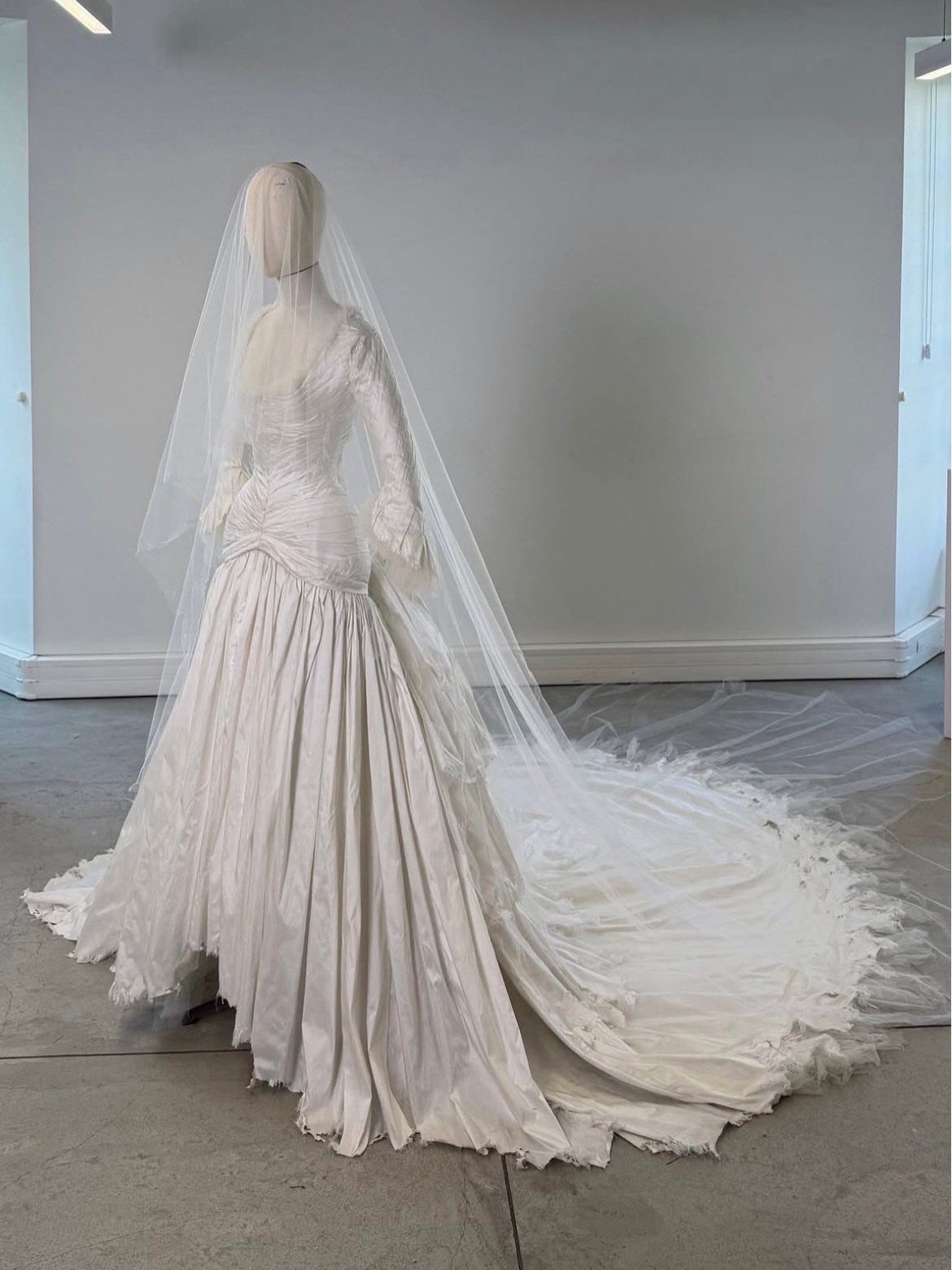 A white wedding dress with a long train and sheer veil displayed on a mannequin.