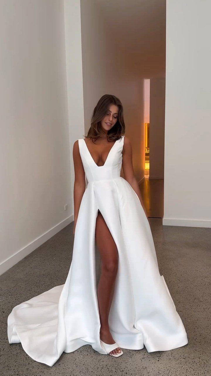 Woman in a white satin wedding dress with a deep plunging neckline and high slit.