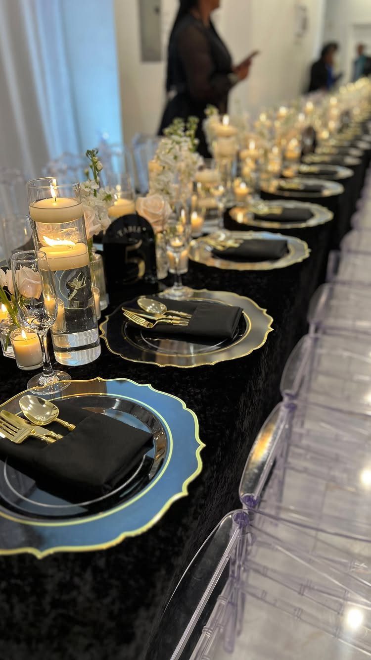 A long banquet table set with black napkins, gold cutlery, and many glowing candles.
