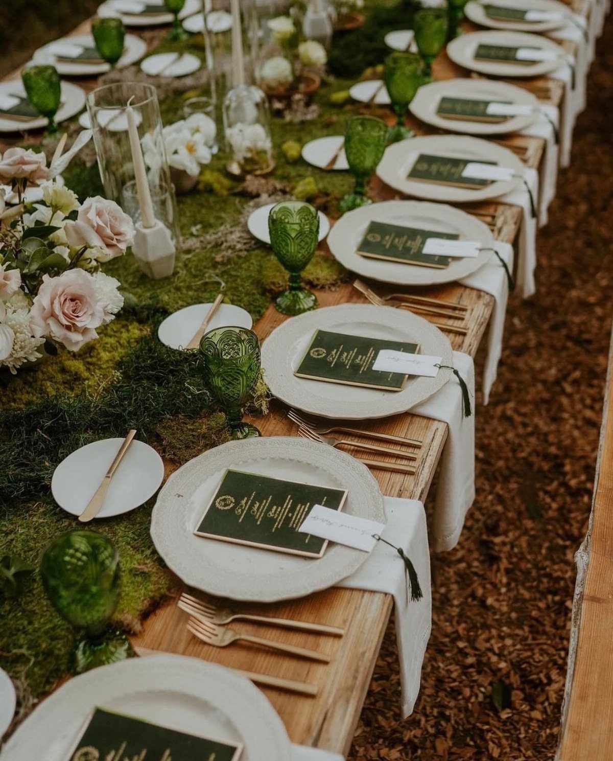 Enchanted Forest Wedding Theme: 10 Ideas for a Natural Setting 4 A long wooden wedding table decorated with green moss, white roses, green glassware, and wooden cutlery.