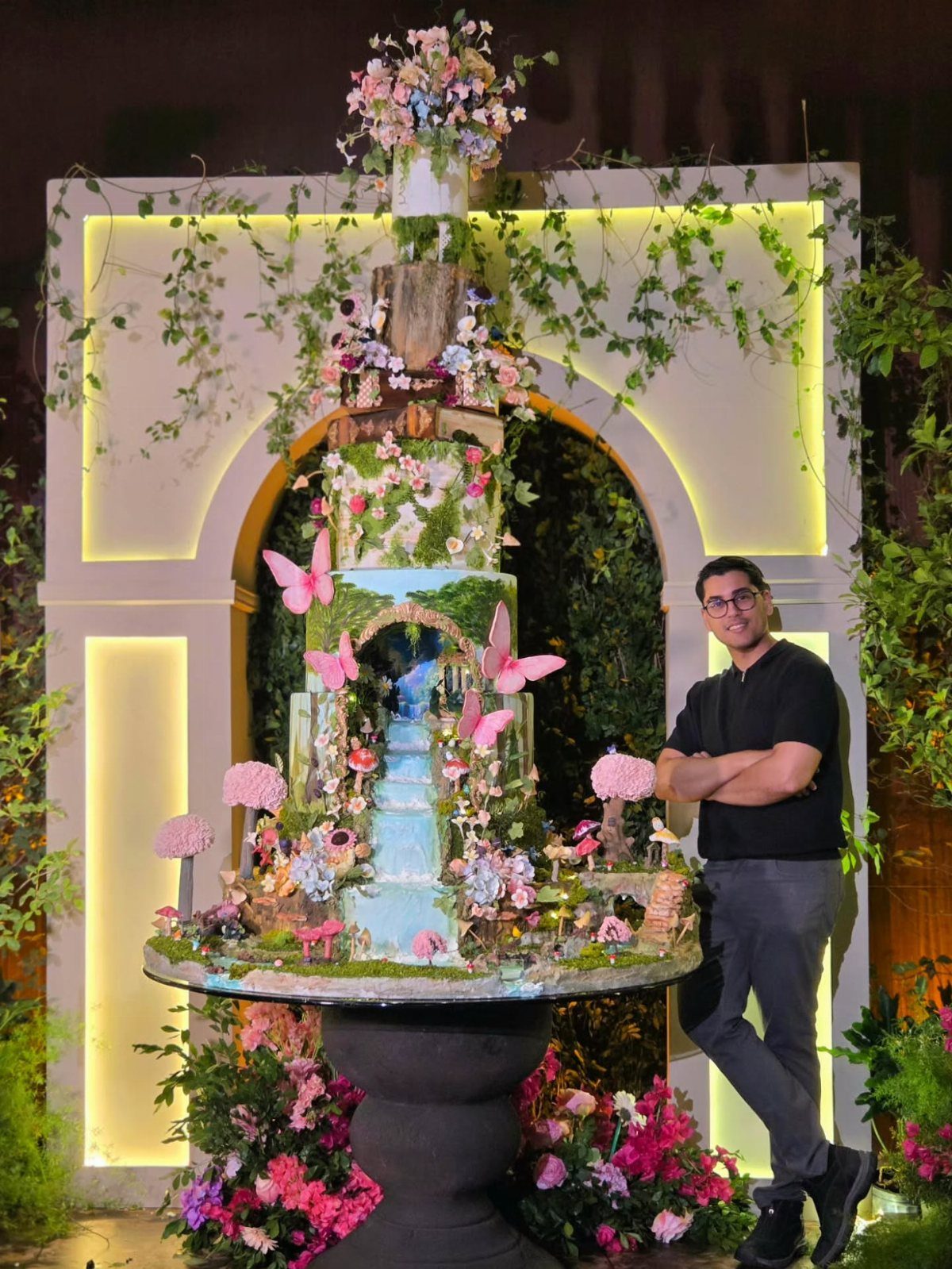 Enchanted Forest Wedding Theme: 10 Ideas for a Natural Setting 6 A tall, multi-tiered enchanted forest wedding cake decorated with pink butterflies and flowers.