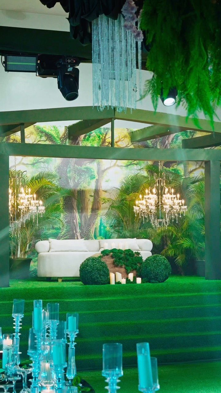 White sofa on green turf surrounded by tropical plants and crystal chandeliers.