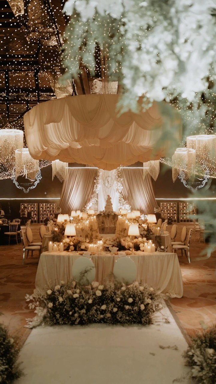 A decorated wedding reception table with glowing candles and fairy lights under a large fabric installation.