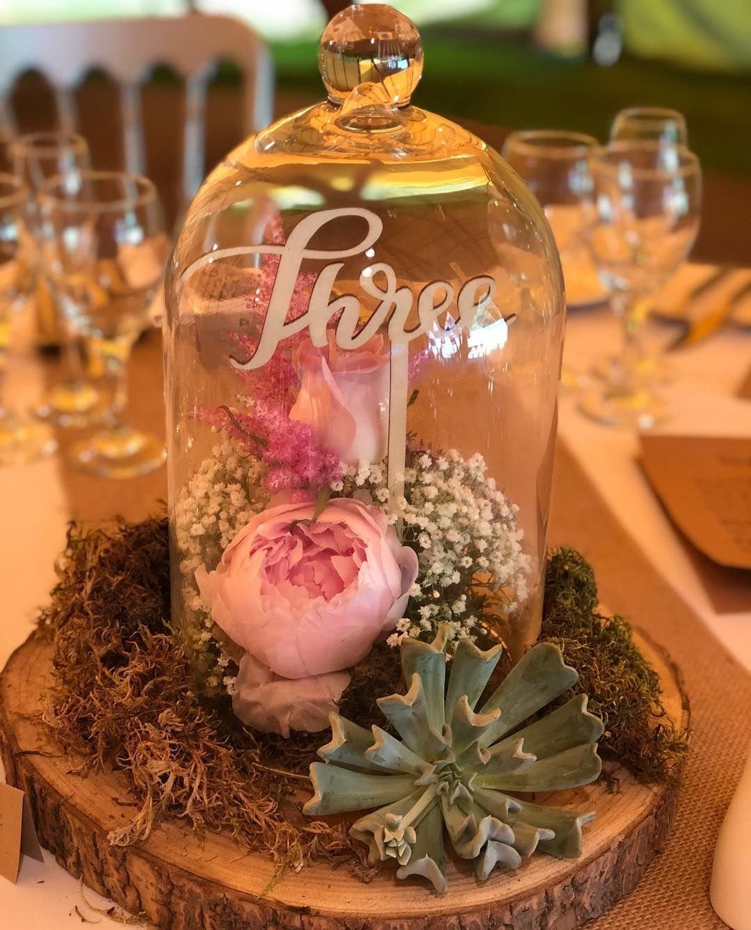 Glass cloche centerpiece with pink peony and moss on a wooden slice.
