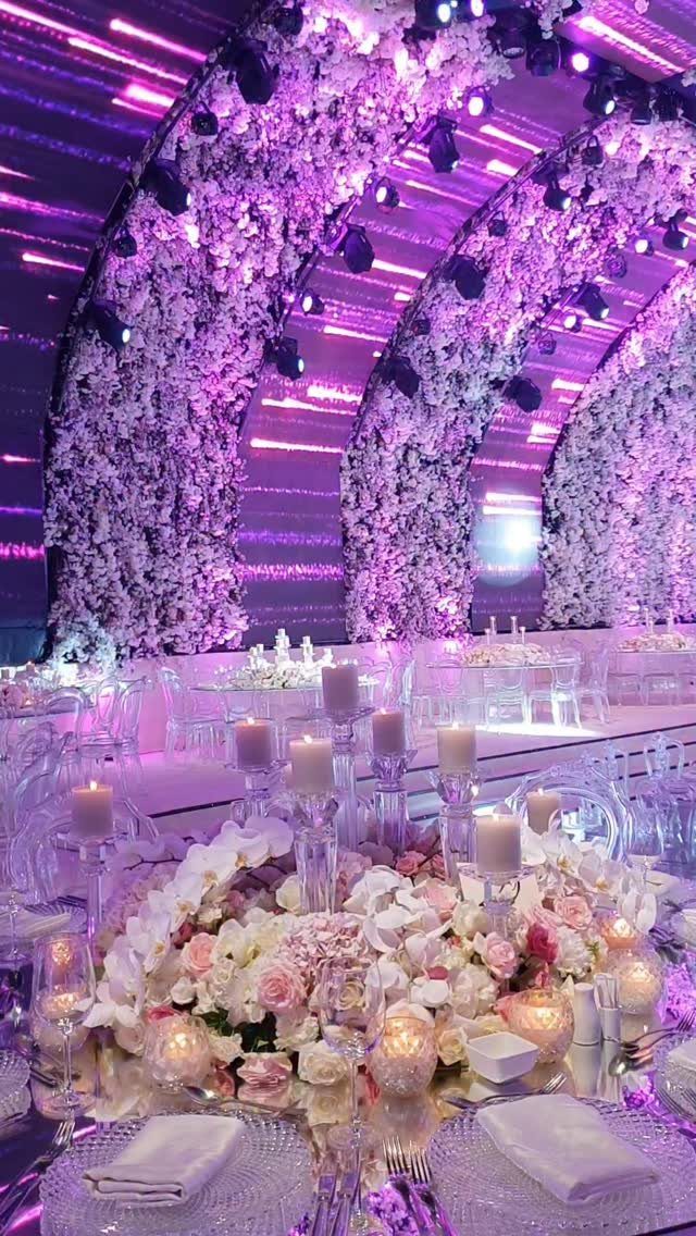 White floral arches illuminated by purple lights over a decorated wedding reception table.