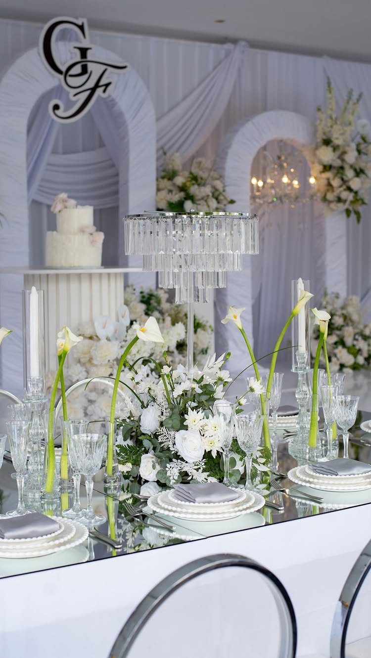 A formal wedding table setting with white flowers and glassware on a mirrored tabletop.