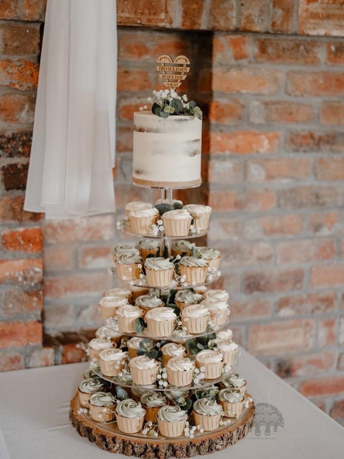 A tiered cupcake display topped with a small naked wedding cake and greenery.