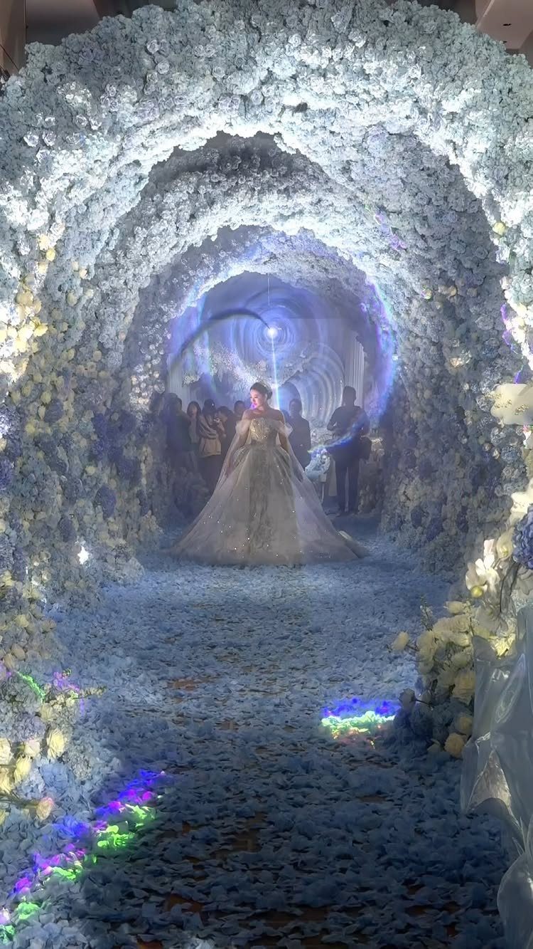 A woman in a large princess wedding dress walking through a floral tunnel.