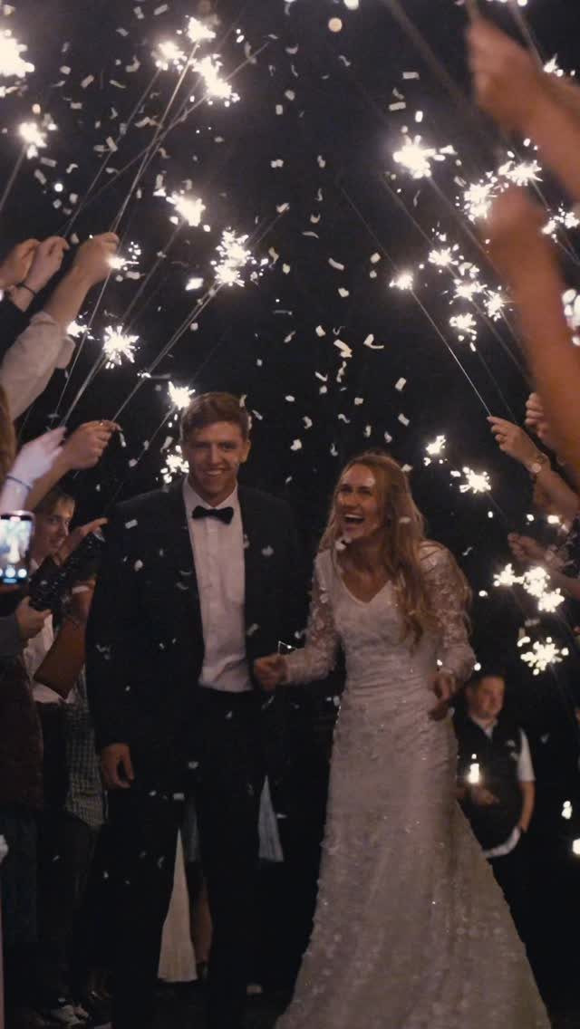 Bride and groom walking through a tunnel of guests holding glowing sparklers at night.