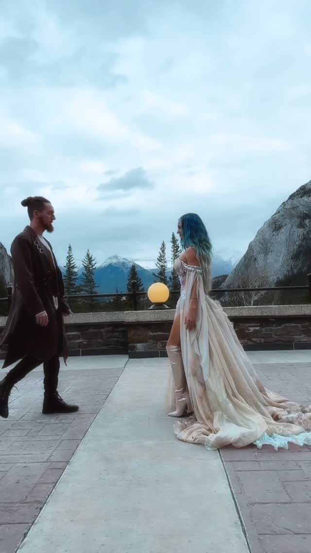 A man and a woman in ethereal fantasy attire walking on a mountain terrace.