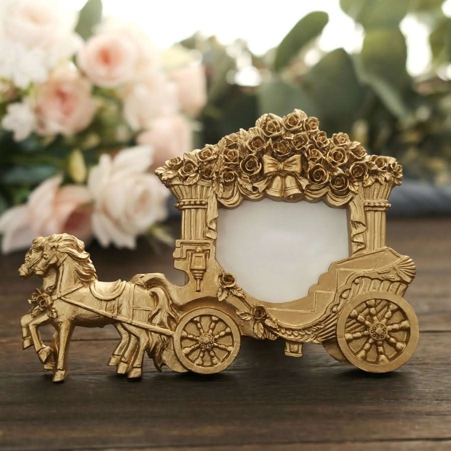 A gold horse-drawn carriage photo frame decorated with roses on a wooden surface.