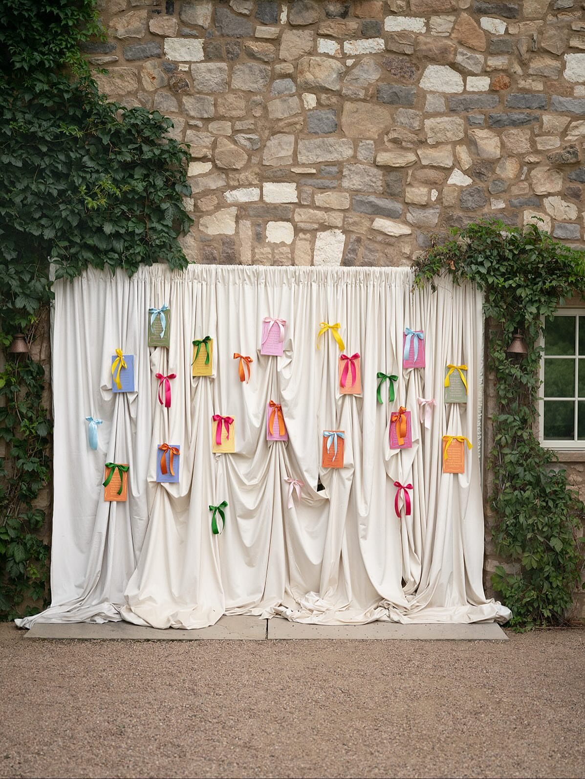 Colorful small bags hanging on a draped white fabric backdrop against a stone wall.