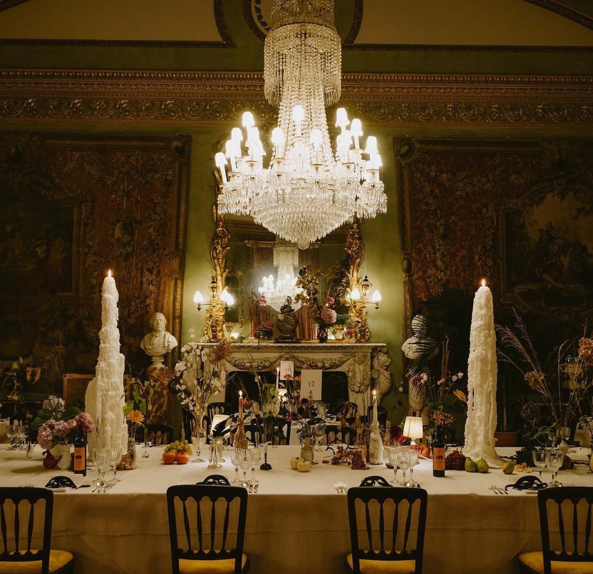 Gothic Wedding Theme: 11 Dark & Elegant Ideas 1 A formal dining table set with tall white candles under a large crystal chandelier.