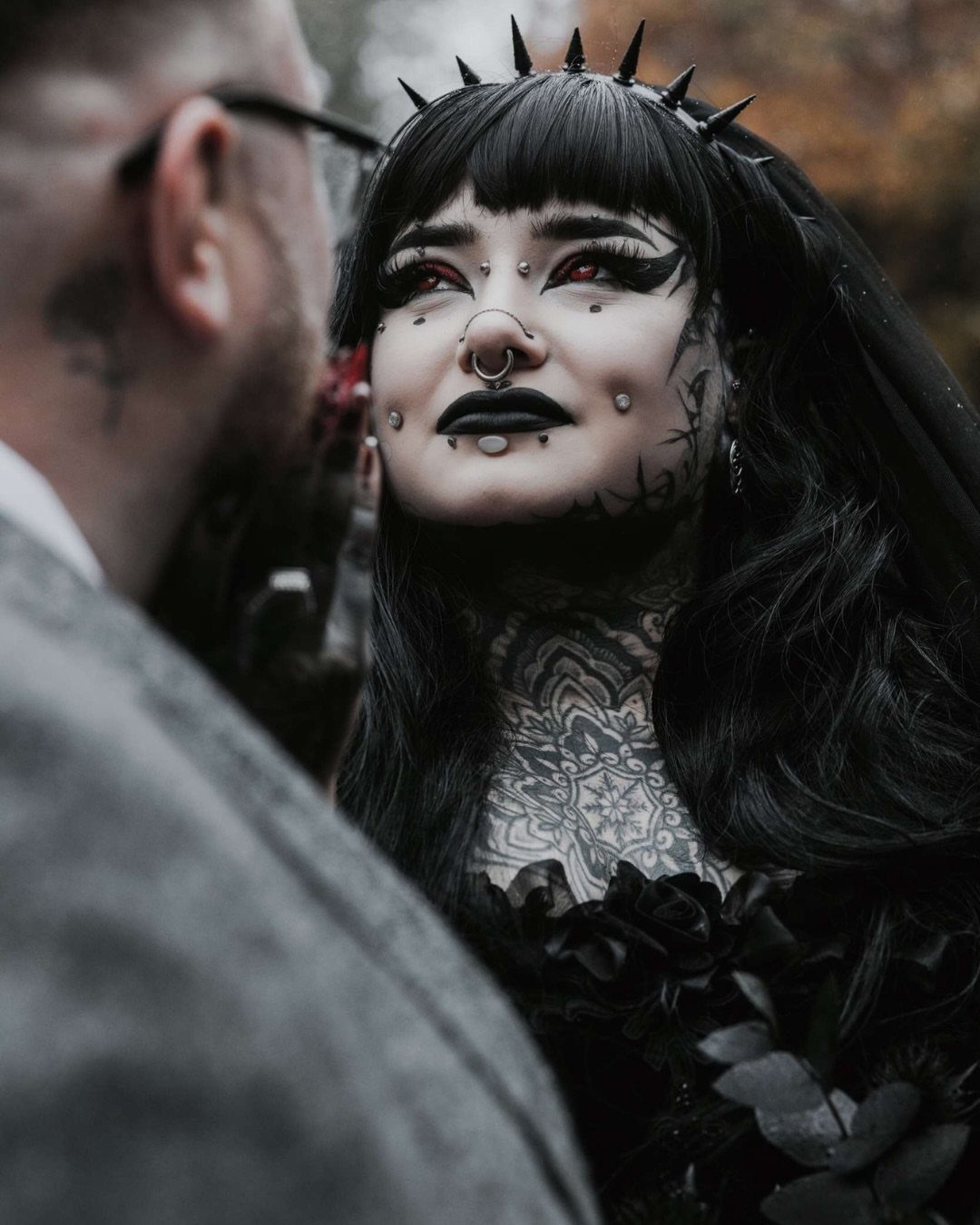 Gothic Wedding Theme: 11 Dark & Elegant Ideas 7 Gothic bride with heavy black makeup and facial piercings looking up at a man outdoors.