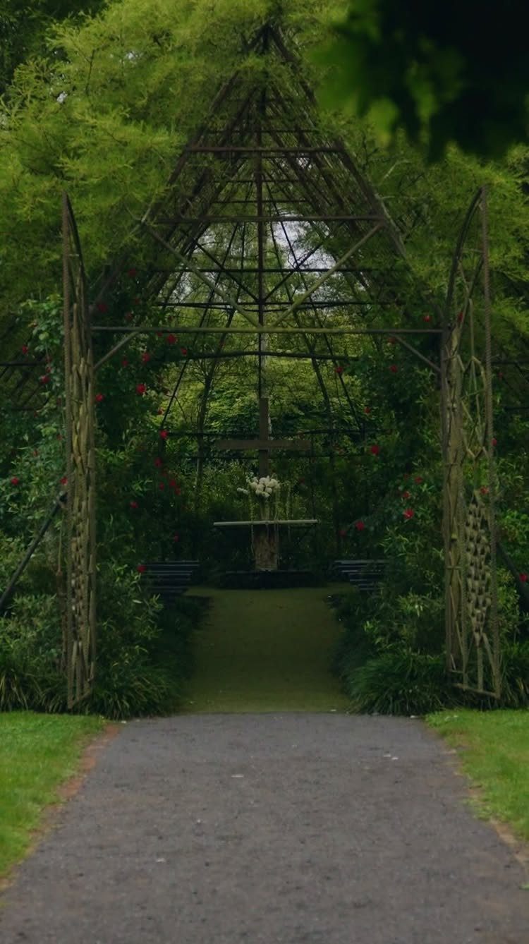 Gothic Wedding Theme: 11 Dark & Elegant Ideas 11 A dark metal garden trellis archway covered in green vines and red flowers over a path.