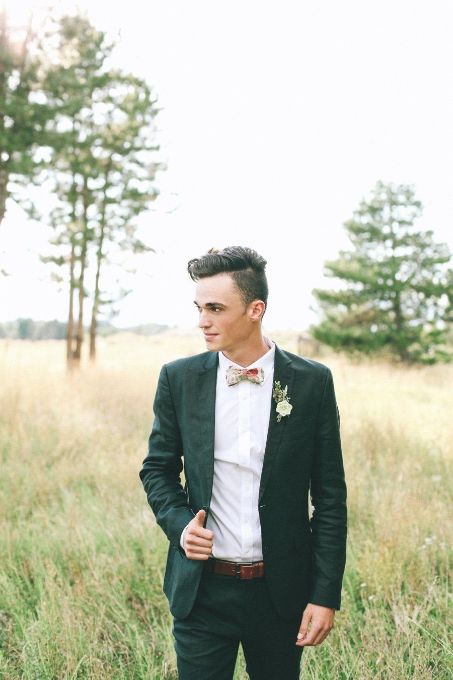 Green Wedding Suit: 8 Looks for Grooms and Guests 7 A man wearing a dark green suit and a white floral boutonniere standing in a field.