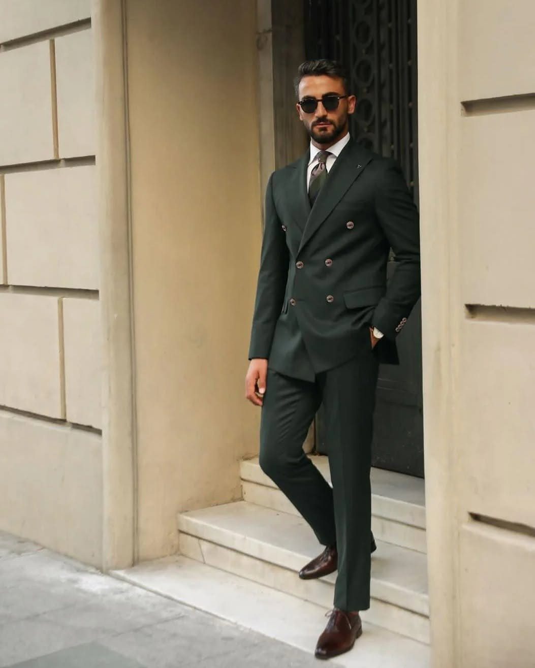 Green Wedding Suit: 8 Looks for Grooms and Guests 3 Man in a forest green double-breasted tailored suit posing by a stone doorway.