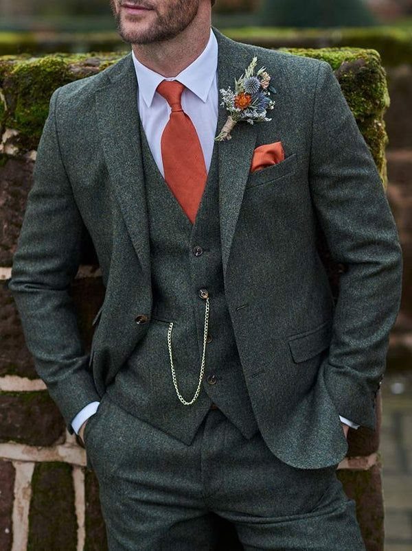 Green Wedding Suit: 8 Looks for Grooms and Guests 6 A man posing in a dark green textured wool three-piece suit with an orange tie.