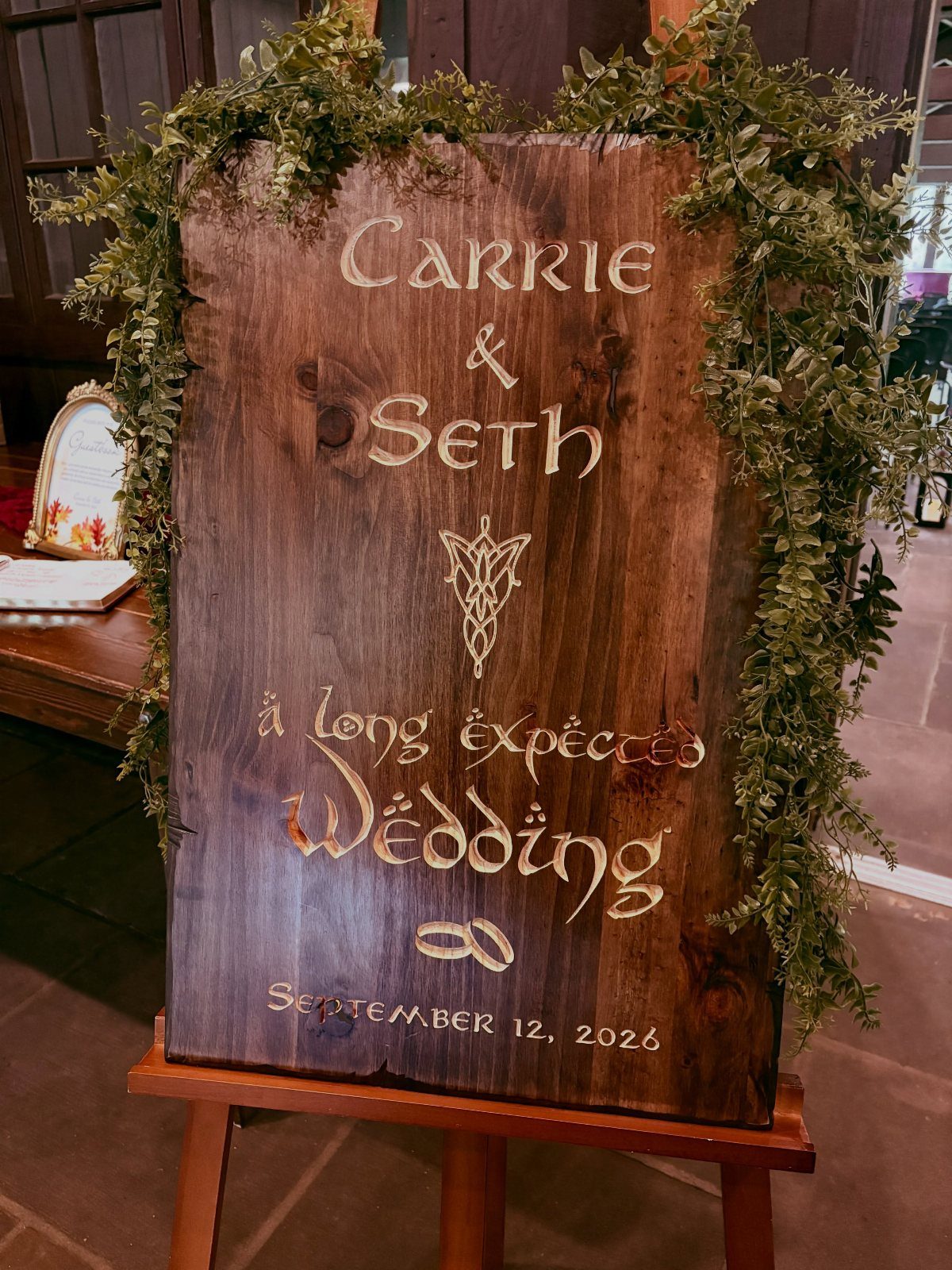 Hobbit Themed Wedding: 20 Ideas for Your Shire Celebration 13 A rustic wooden wedding sign with fantasy lettering and green leafy vine decorations on an easel.