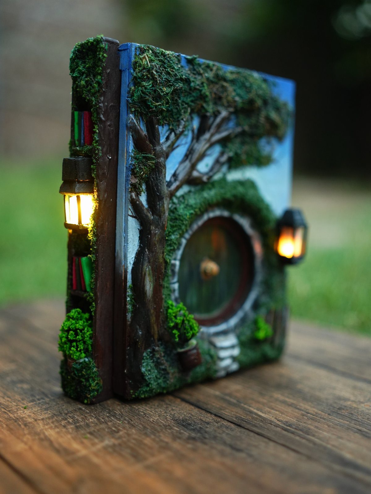 Hobbit Themed Wedding: 20 Ideas for Your Shire Celebration 6 A Hobbit-themed book decorated with moss, trees, and glowing miniature lanterns on a wooden table.